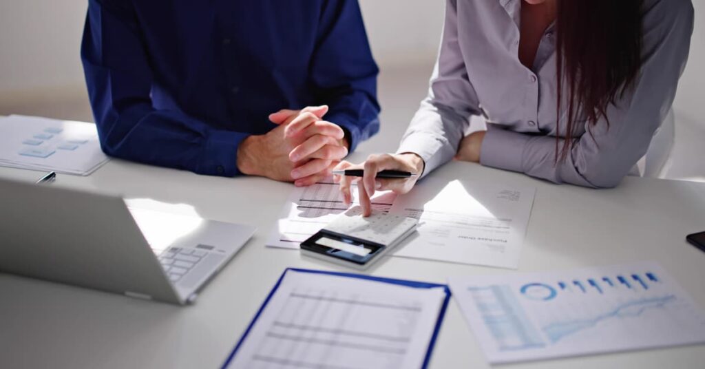 Dos personas revisando facturas y cálculos de impuestos trimestrales con una calculadora y gráficos financieros sobre la mesa.